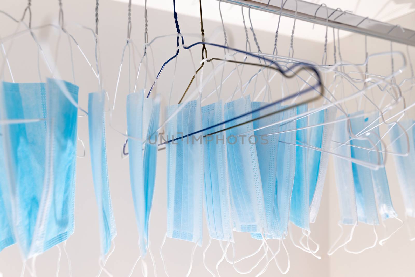Disposable surgical masks hanging on hangers in a wardrobe closet. Concept of new normal. Concept of waring a mask becoming e new habit. Concept of adaptation during crisis and pandemic due to Covid. by dugulan