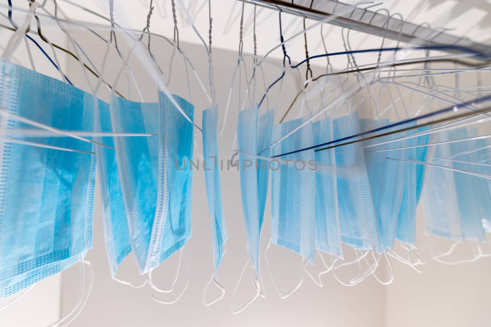 Disposable surgical masks hanging on hangers in a wardrobe closet. Concept of new normal. Concept of waring a mask becoming e new habit. Concept of adaptation during crisis and pandemic due to Covid. by dugulan