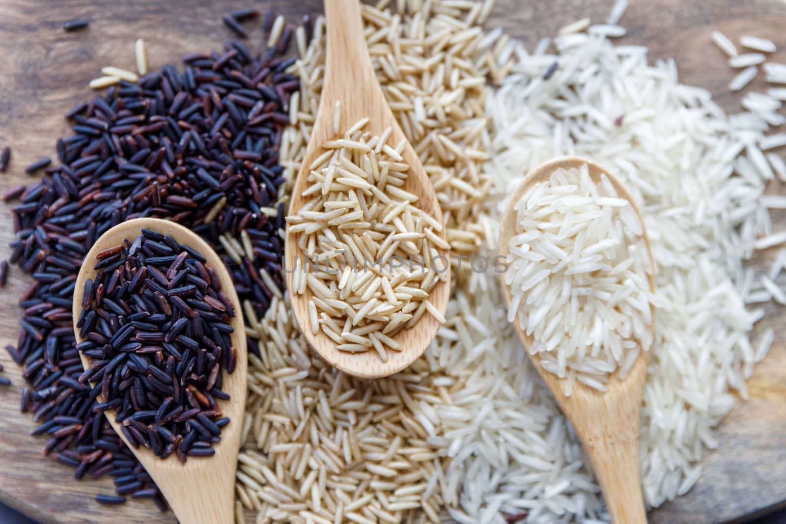 Black wild rice, brown wild rice and white jasmine rice in wooden spoon flat lay. Creative layout. Food concept.