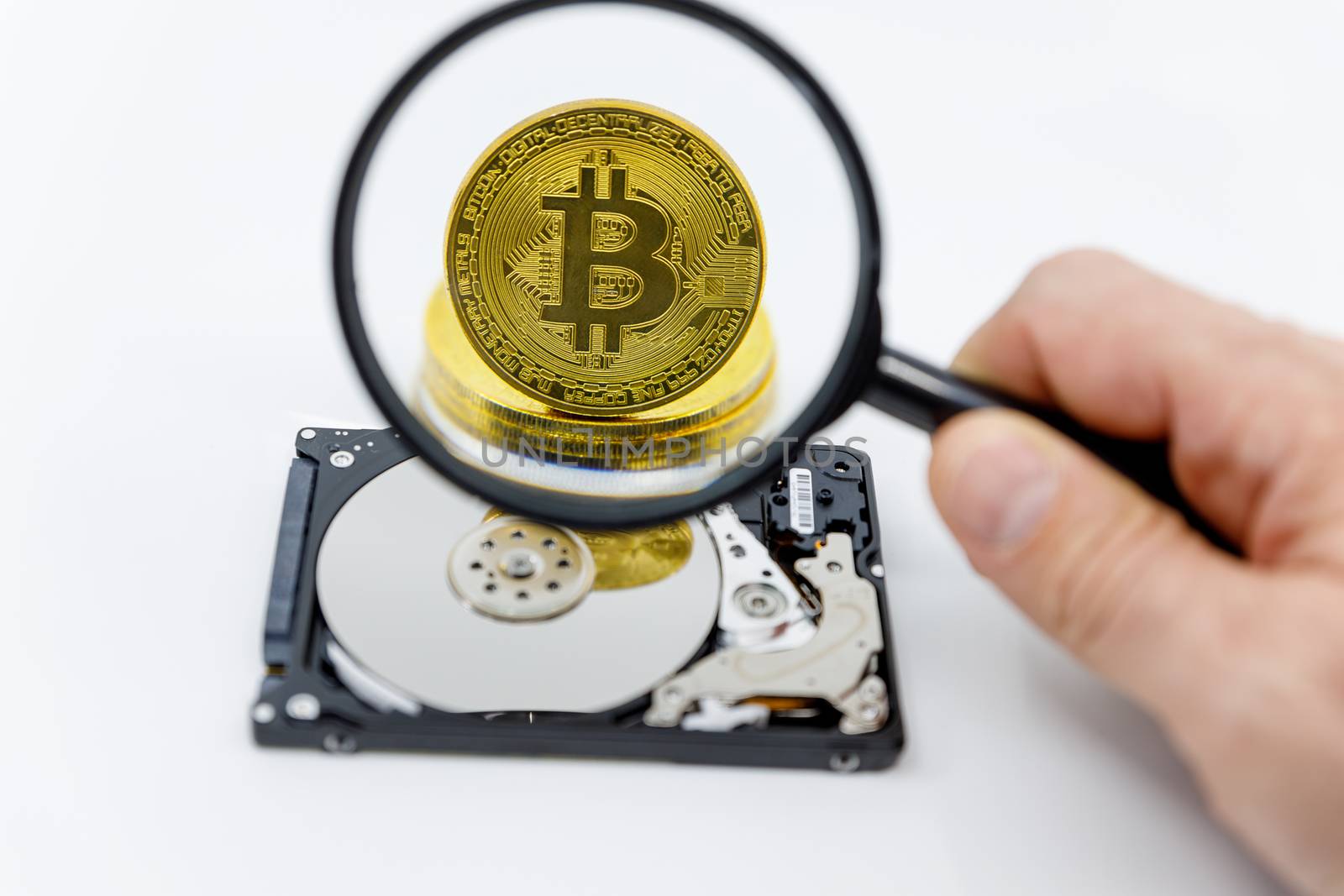 Magnifying glass over a gold bitcoin token on top of an open hard drive.Worldwide virtual internet cryptocurrency and digital payment system.Digital coin money crypto currency by dugulan