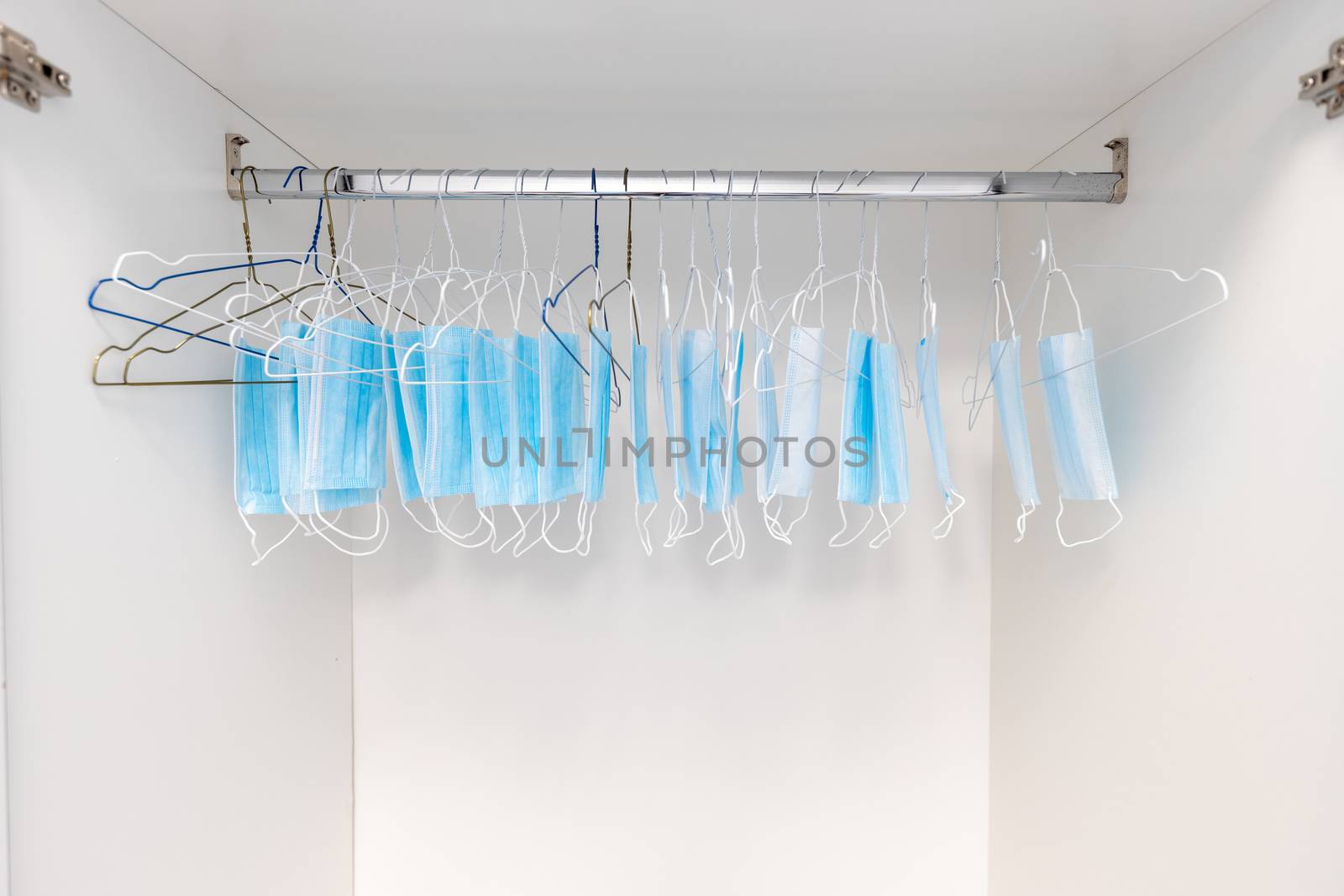 Disposable surgical masks hanging on hangers in a wardrobe closet. Concept of new normal. Concept of waring a mask becoming e new habit. Concept of adaptation during crisis and pandemic due to Covid.