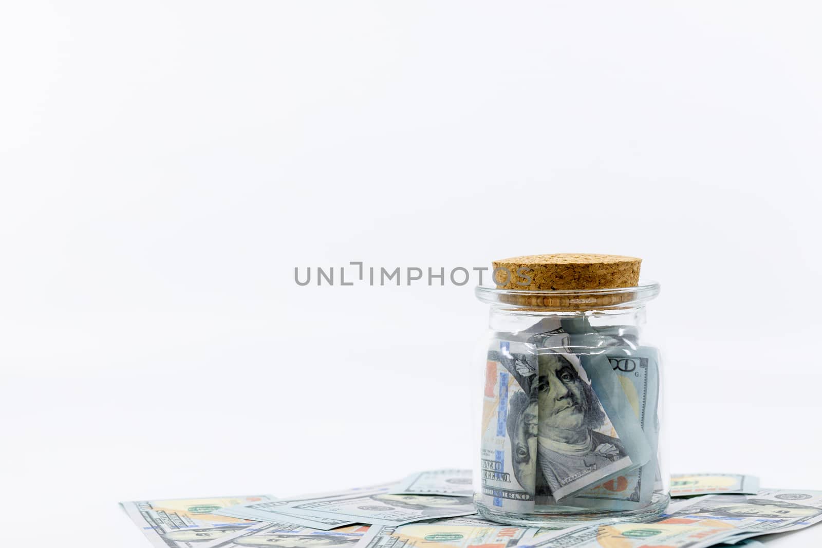 Jar full and over flowing with hundred dollar bill banknotes sitting on big pile of money. White negative space, copy space. Concept saving money for finance accounting, retirement, schooling.