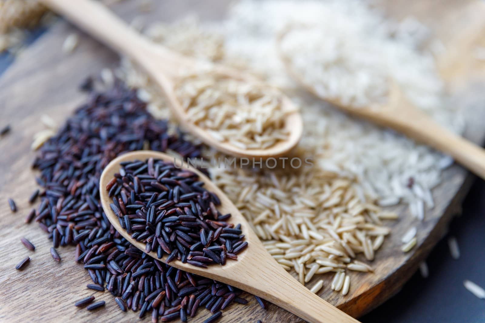 Black wild rice, brown wild rice and white jasmine rice in wooden spoon flat lay. Creative layout. Food concept. Focus on black rice. by dugulan
