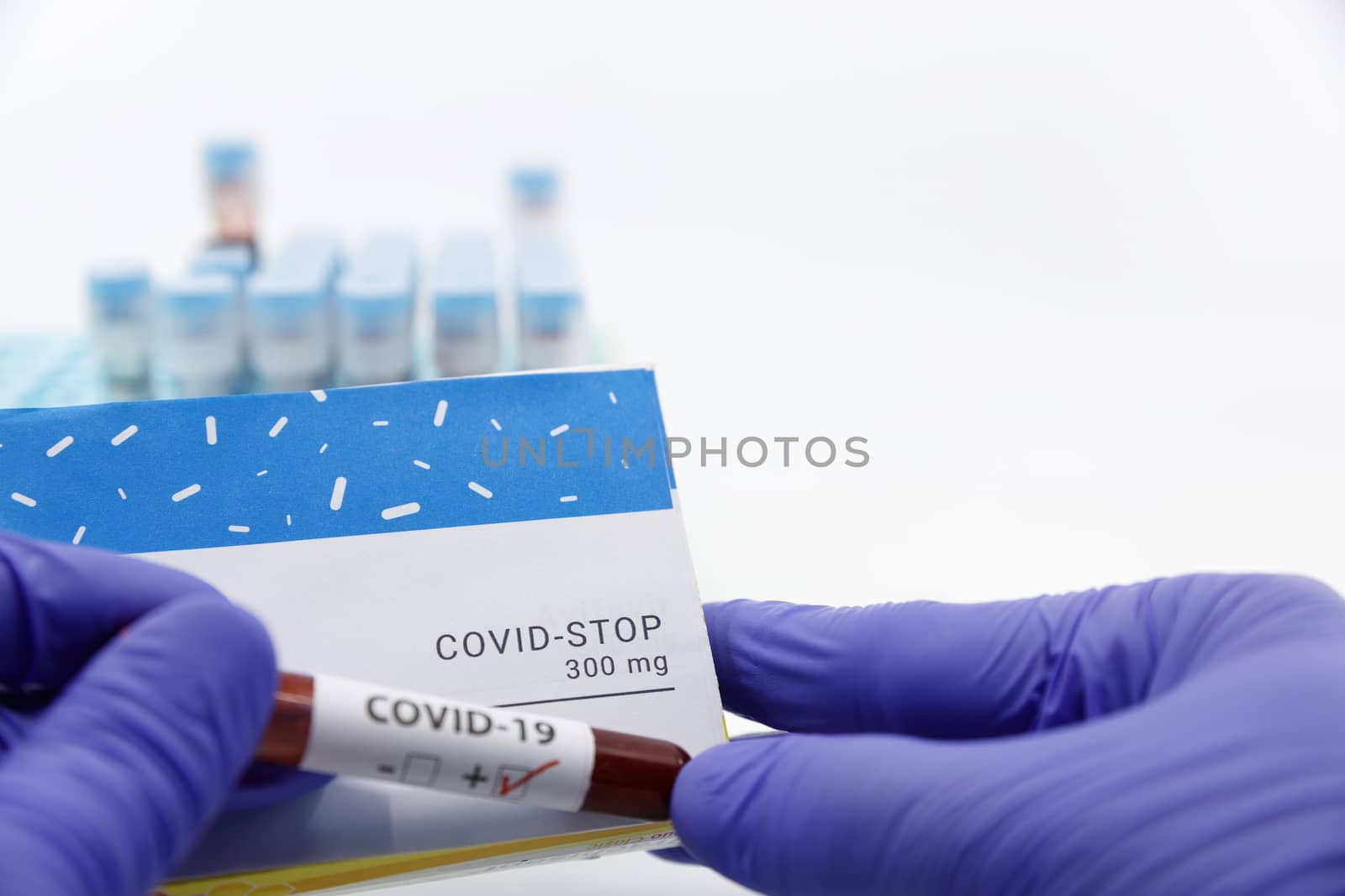 Doctor showing box of medicine with positive covid-19 test.Concept of covid stop medicine with blood tests tubes on the background.Cure for coronavirus,COVID-19 treatment.