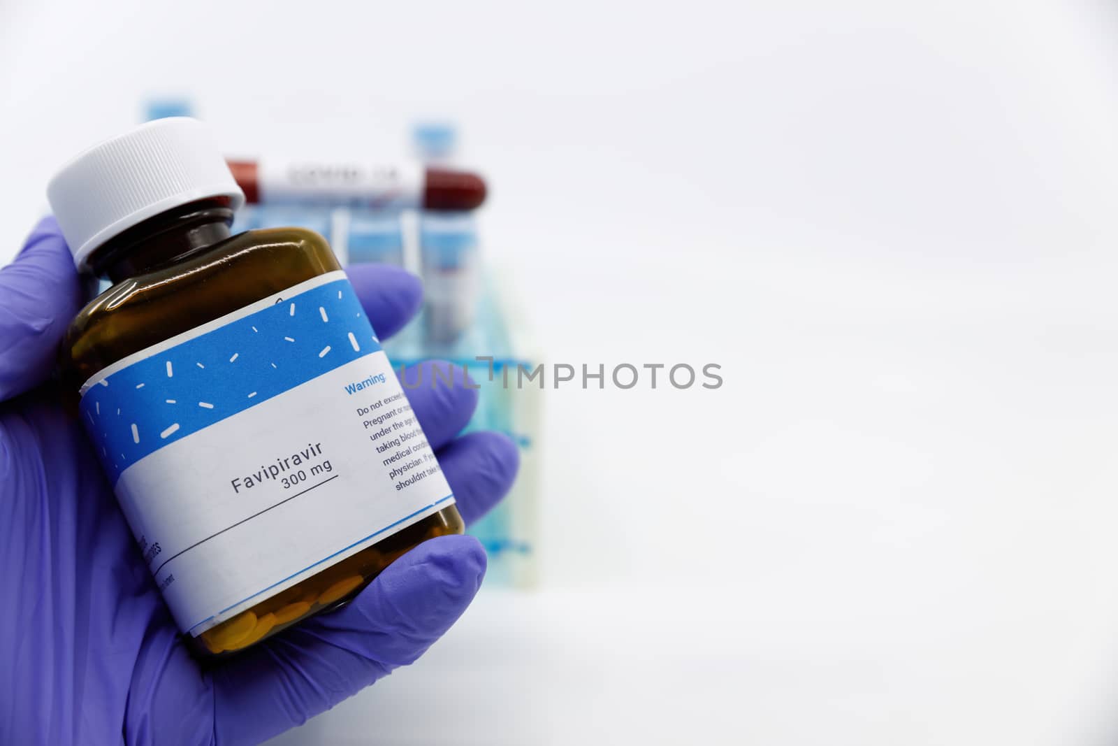Dubai-UAE-Circa 2020:Doctor showing bottle of medicine for covid-19 treatment.Concept of Favipiravir medicine with blood tests tubes on the background.Cure for coronavirus,COVID-19 treatment. by dugulan