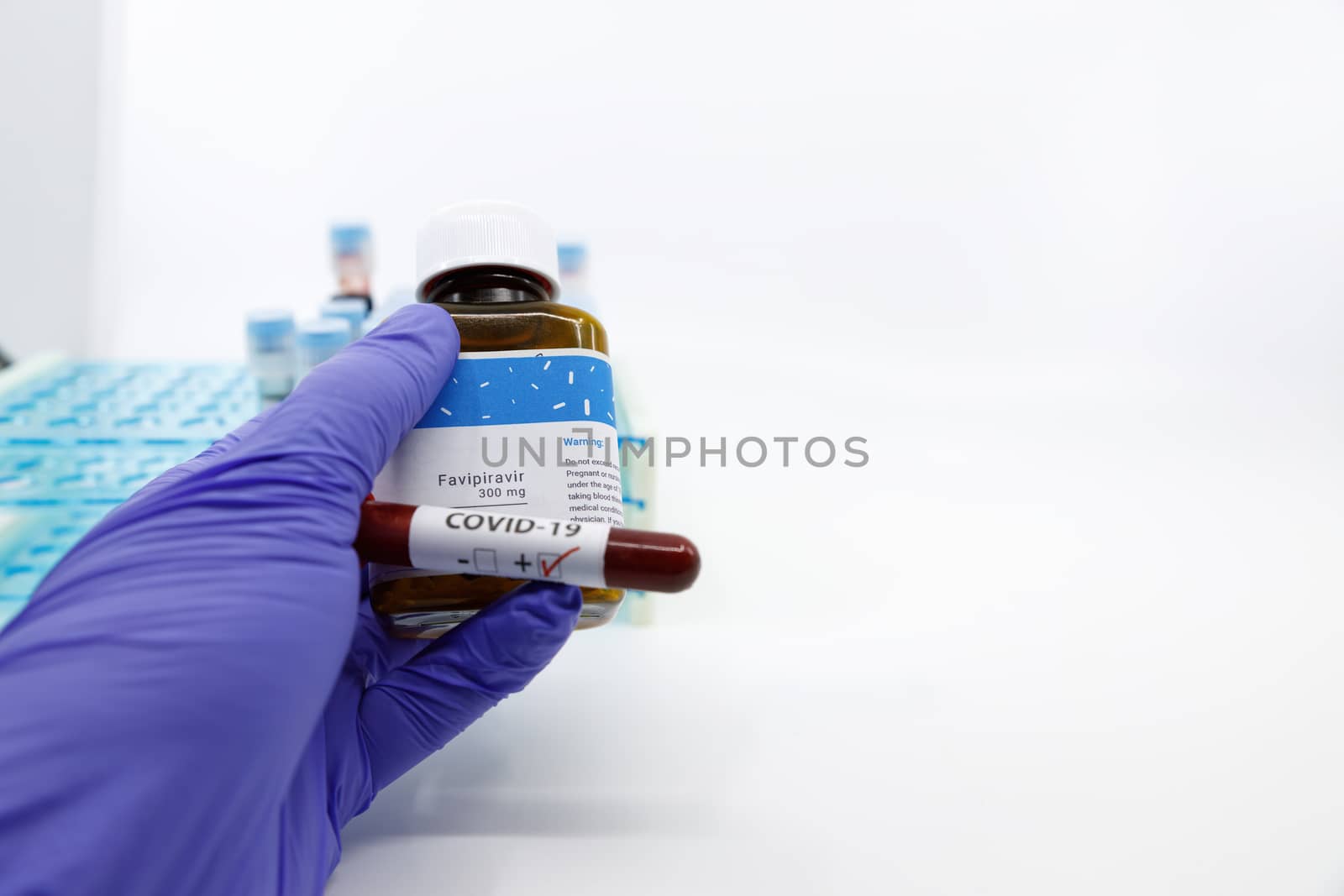 Dubai-UAE-Circa 2020:Doctor showing bottle of medicine with positive covid-19 test.Concept of Favipiravir medicine with blood tests tubes on the background.Cure for coronavirus,COVID-19 treatment.