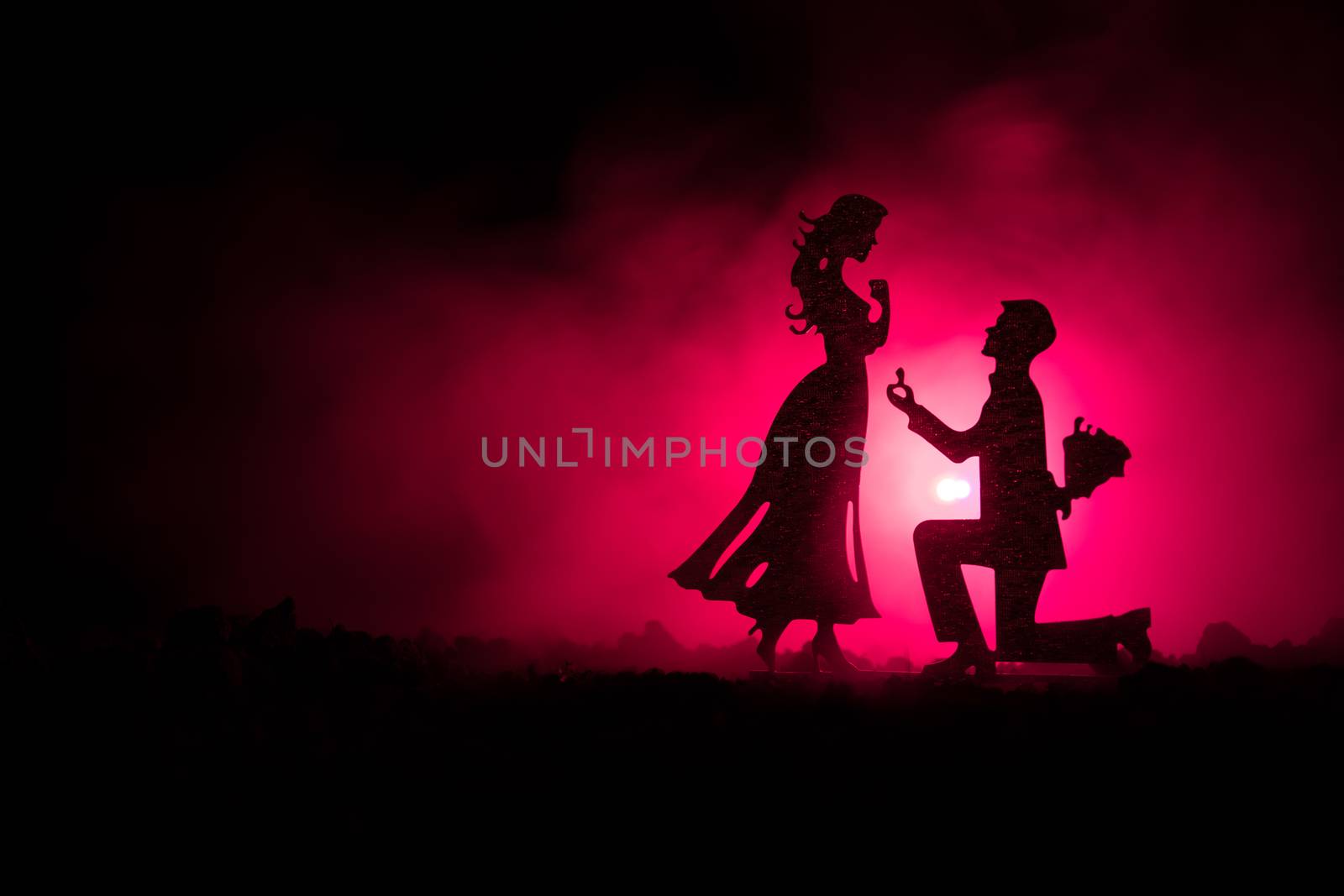 Will you marry me? Silhouette of young man staying on the knee and making proposal for his lovely girl against dark toned background. Valentine greeting card decor. Selective focus