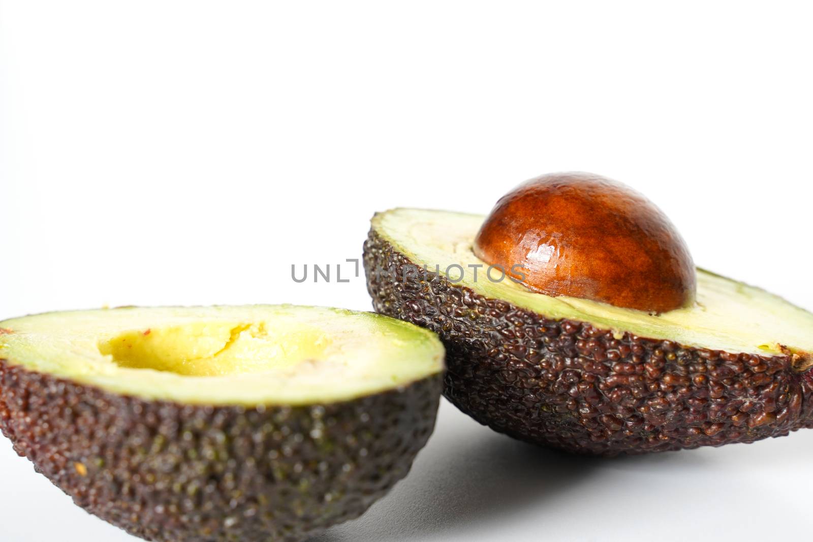 An avocado sliced in half to reveal the core against a plain whit background