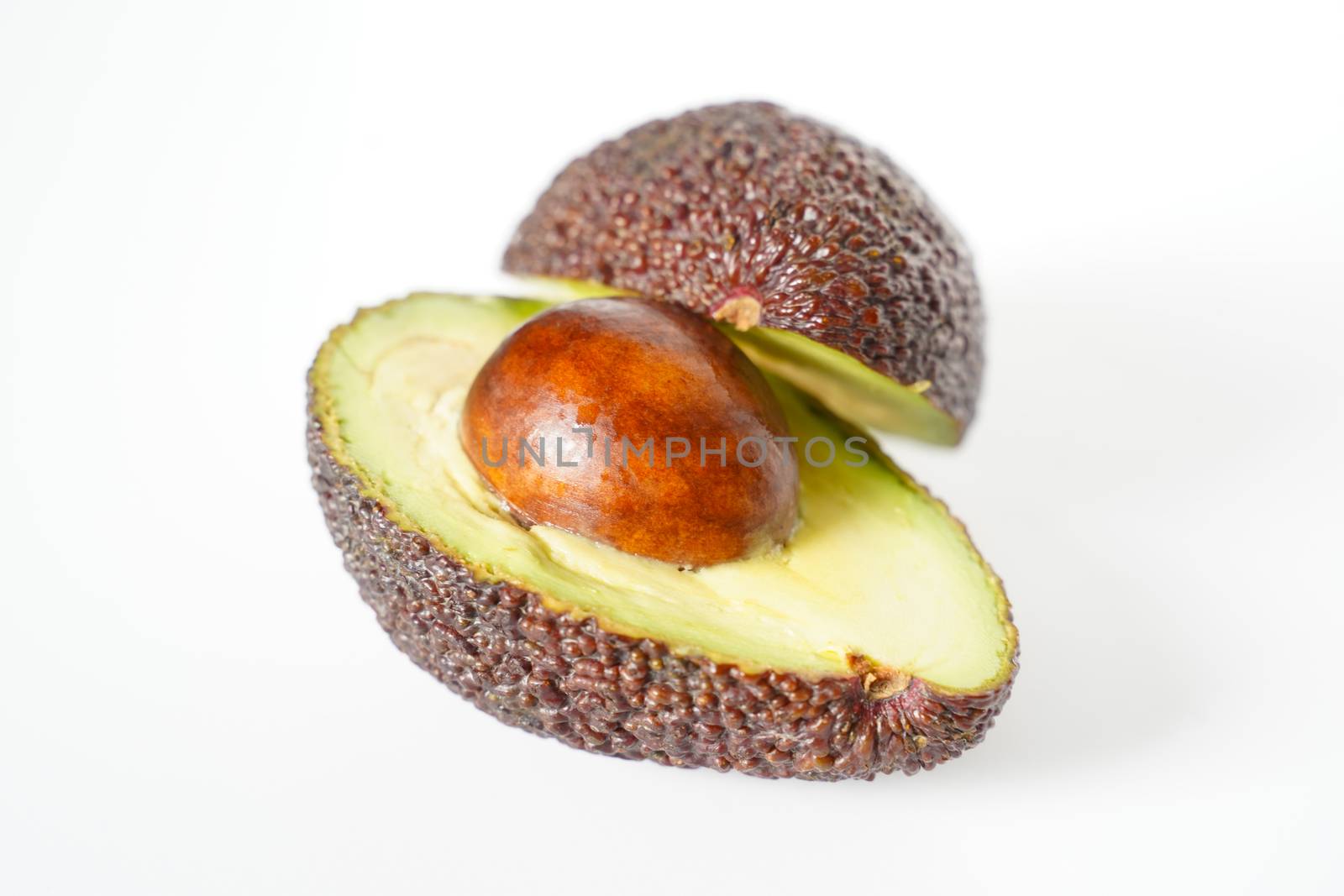 An avocado sliced in half to reveal the core against a plain whit background