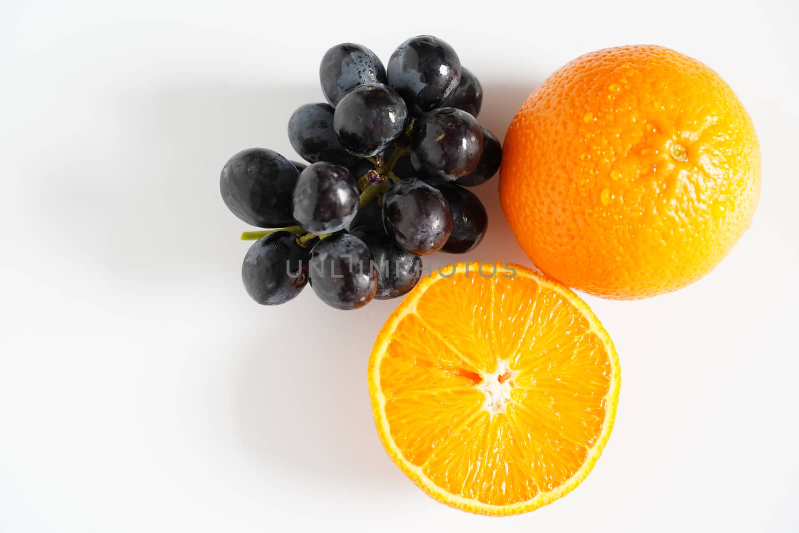 An orange sliced in half and a bunch of black grapes against a plain white background
