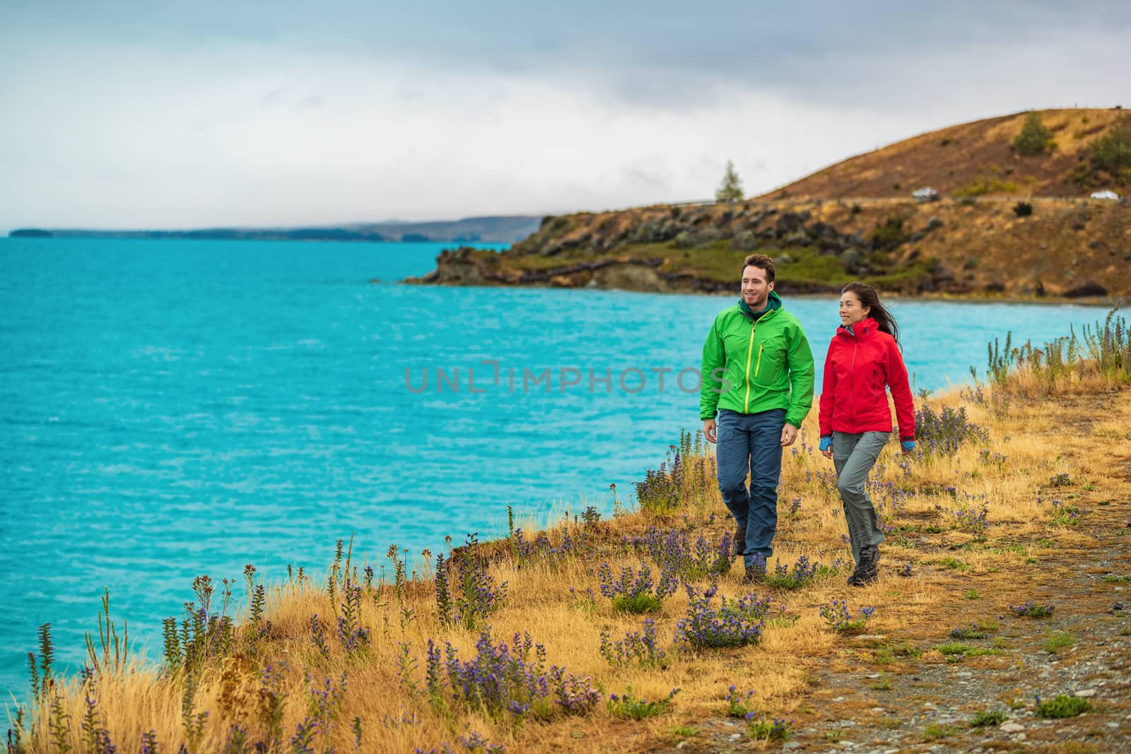 Active people in outdoor activity. Couple tourists hiking in nature with view of Lake Pukaki near Aoraki aka Mount Cook, a famous tourist destination on New Zealand.