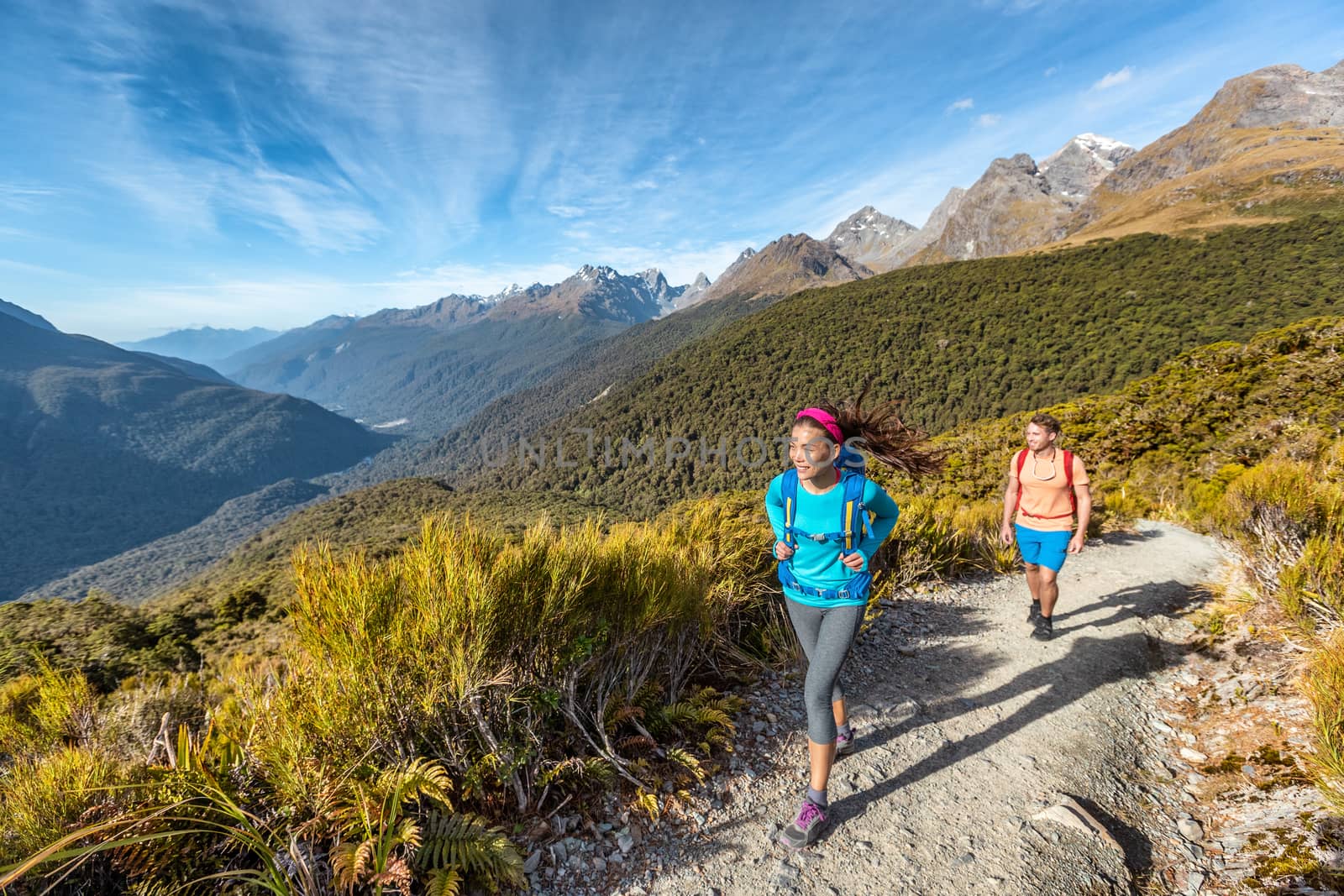 Hiking couple walking on trail at Routeburn Track during sunny day. Male and female hikers are tramping on Key Summit Track. travelling in Fiordland National Park in New Zealand by Maridav