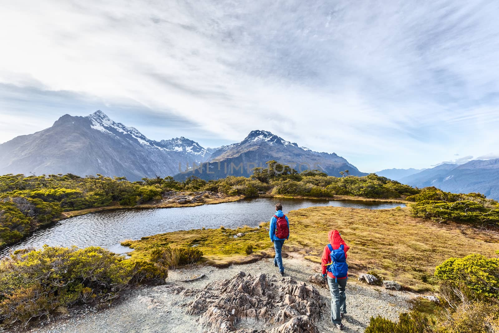 Hiking couple walking on adventure hike at Routeburn Track during sunny day. Hikers carrying backpacks tramping on Key Summit Track. People on vacation at Fiordland National Park, New Zealand by Maridav