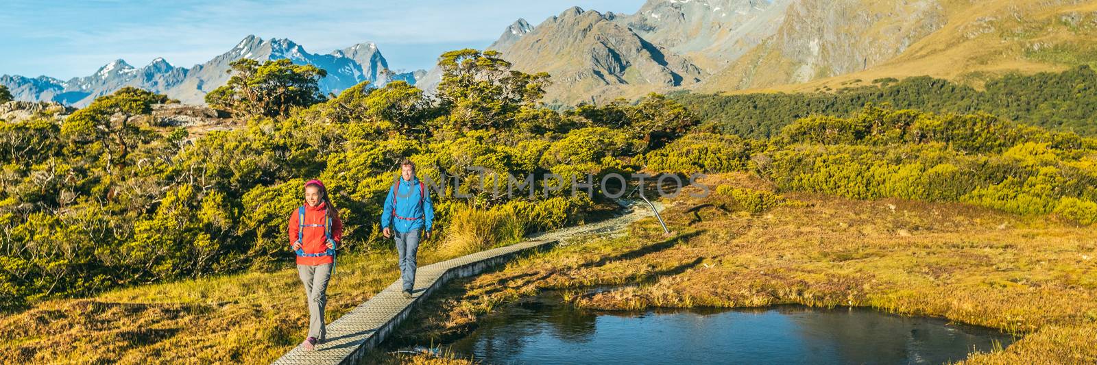 New Zealand Hiking. Panoramic banner of Young hiking couple walking on trail at Routeburn Track during. Hikers carrying backpacks tramping Key Summit Track, Fiordland National Park, New Zealand by Maridav