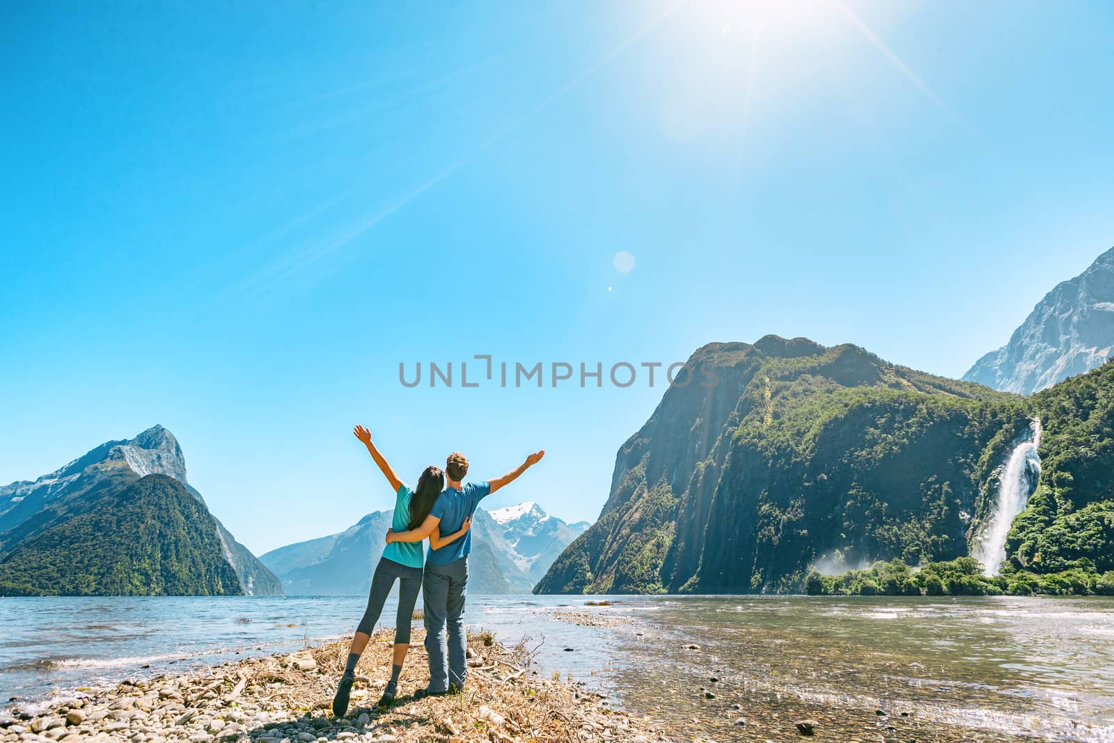 Outdoor couple happy with arms outstretched in Milford Sound New Zealand in nature enjoying active outdoor lifestyle hiking in Milford Sound New Zealand by Mitre Peak in Fiordland by Maridav
