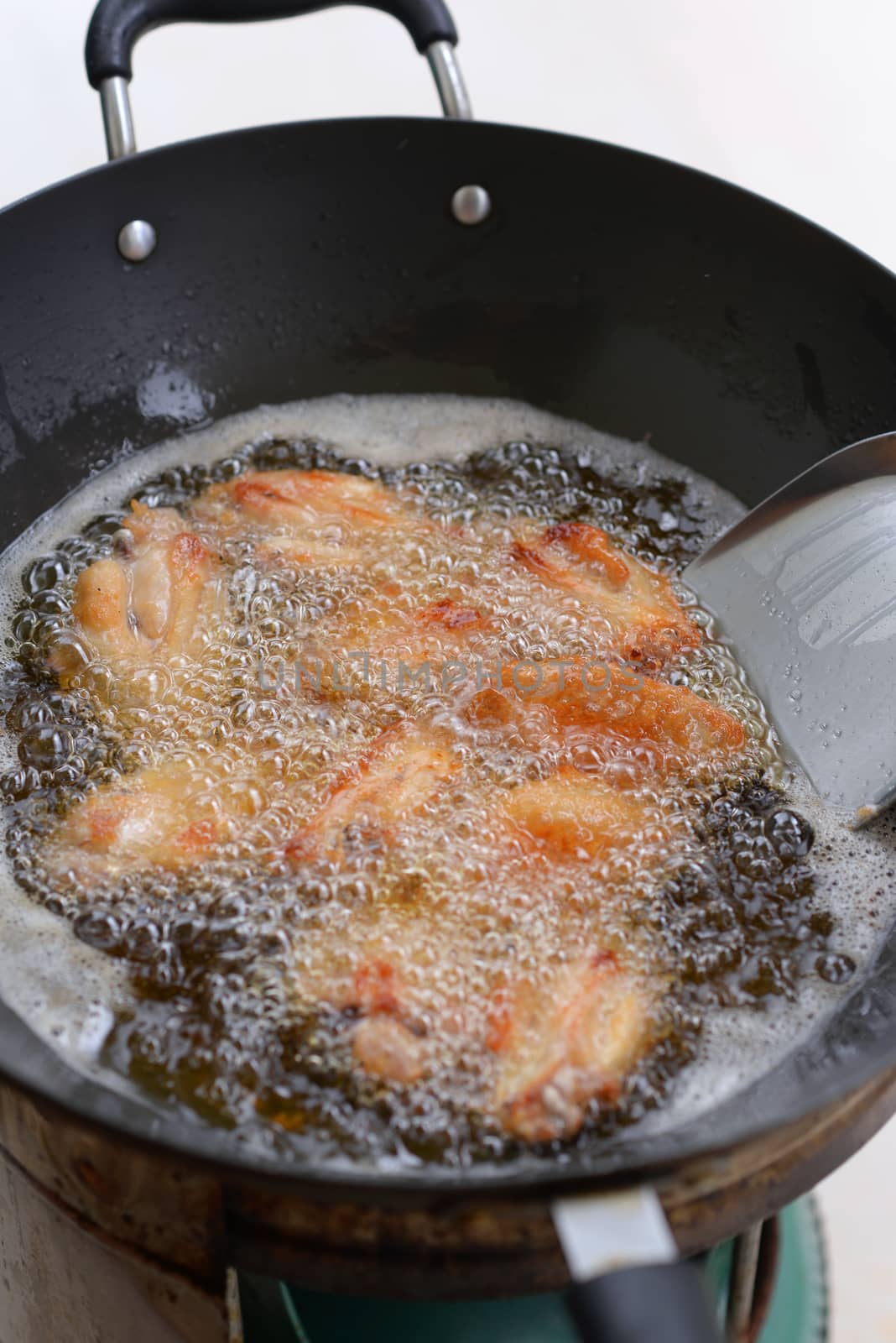 Chicken wings are frying in an iron pan with boiling oil.