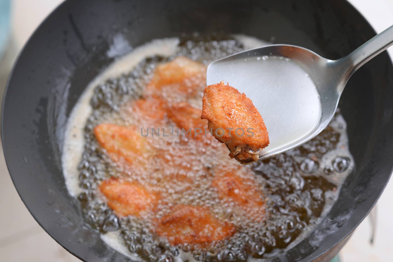 Fried chicken wings cooked on the spatula And the chicken wings in the pan are blurred in the background