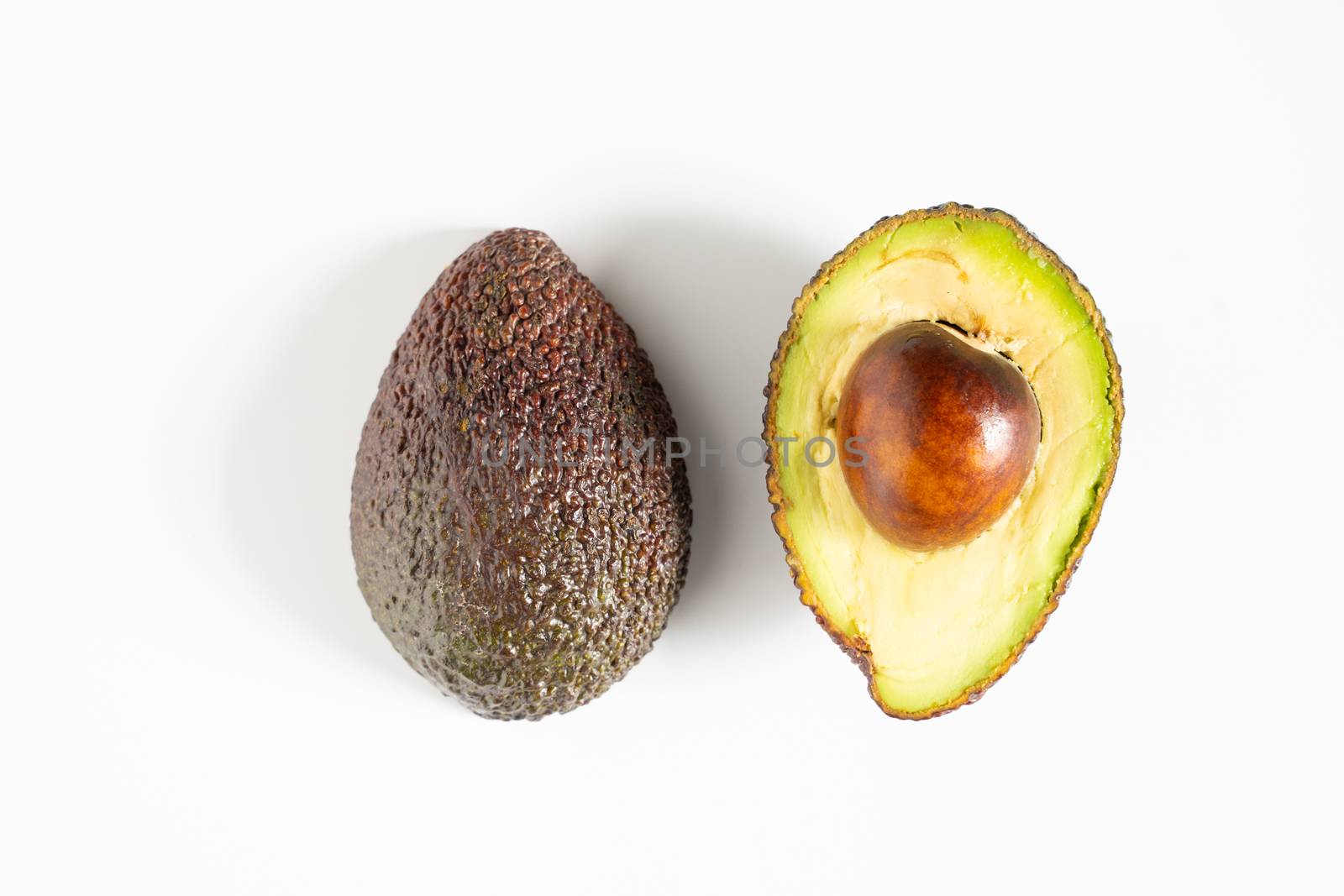 An avocado sliced in half to reveal the core against a plain whit background