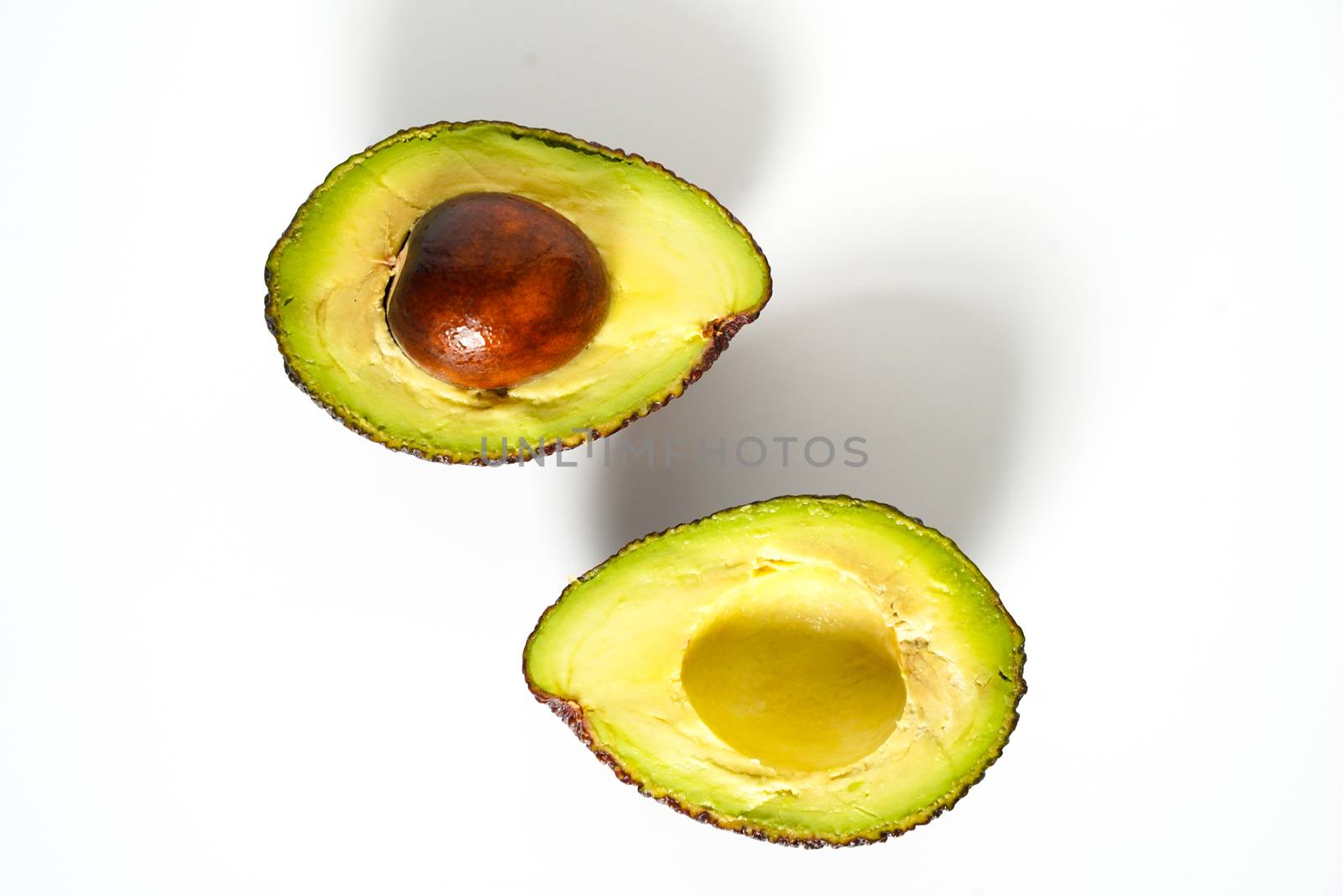 An avocado sliced in half to reveal the core against a plain whit background