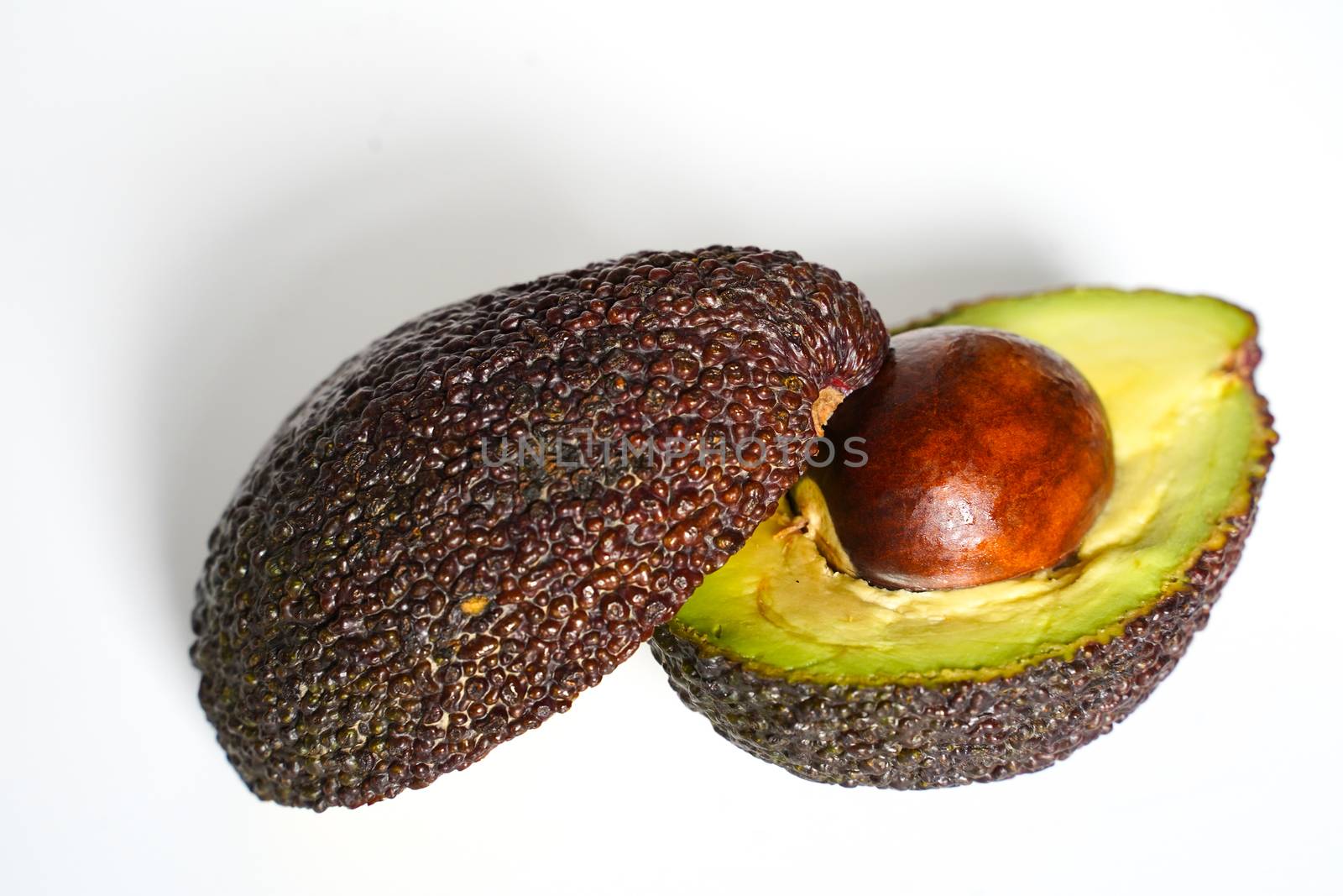 An avocado sliced in half to reveal the core against a plain whit background