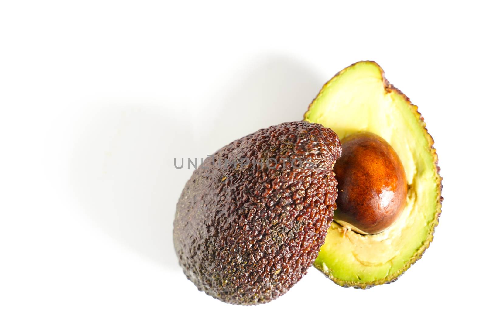 An avocado sliced in half to reveal the core against a plain whit background