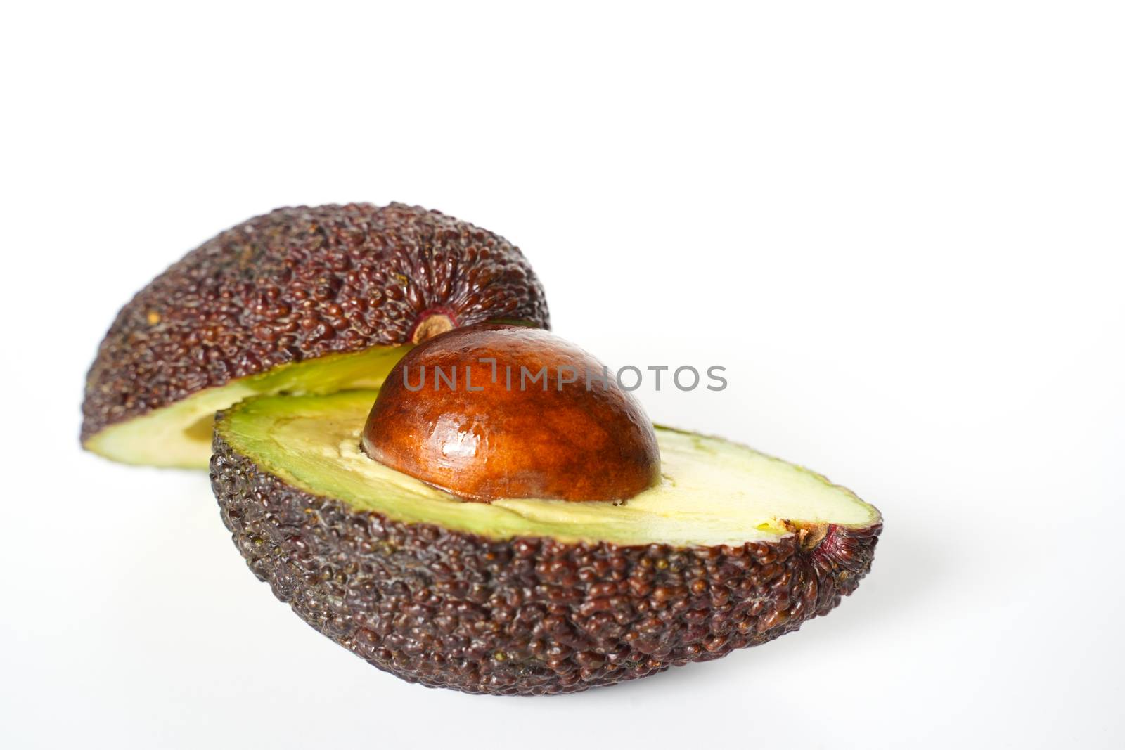 An avocado sliced in half to reveal the core against a plain whit background