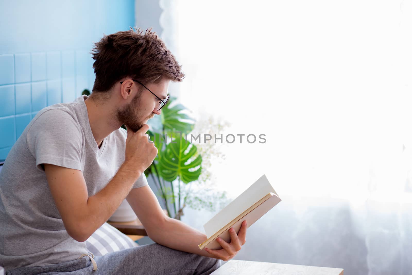 Young man wear glasses reading book on sofa in the living room w by nnudoo