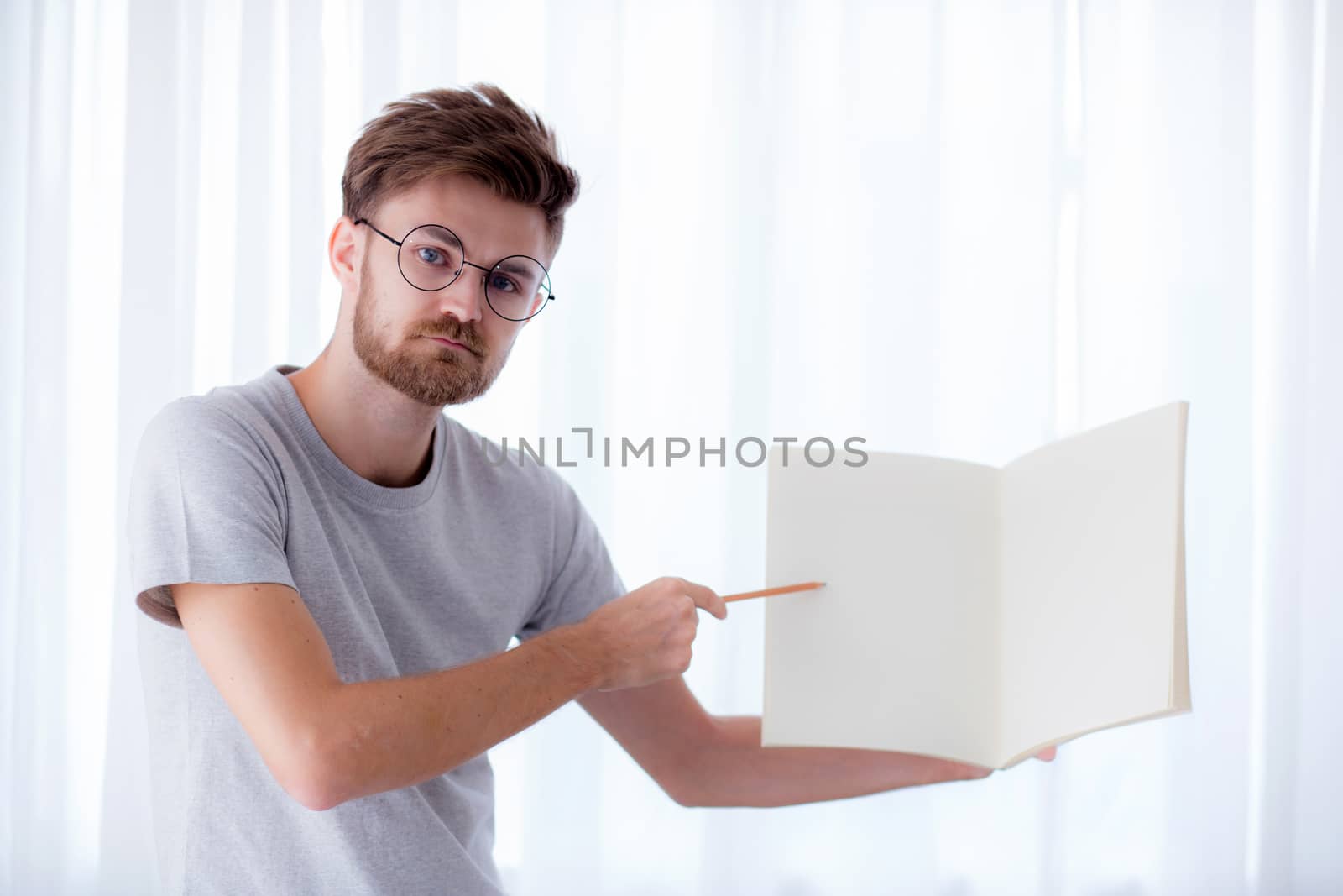 young businessman standing with pencil pointing finger at empty diary with space for text in living room, education concept