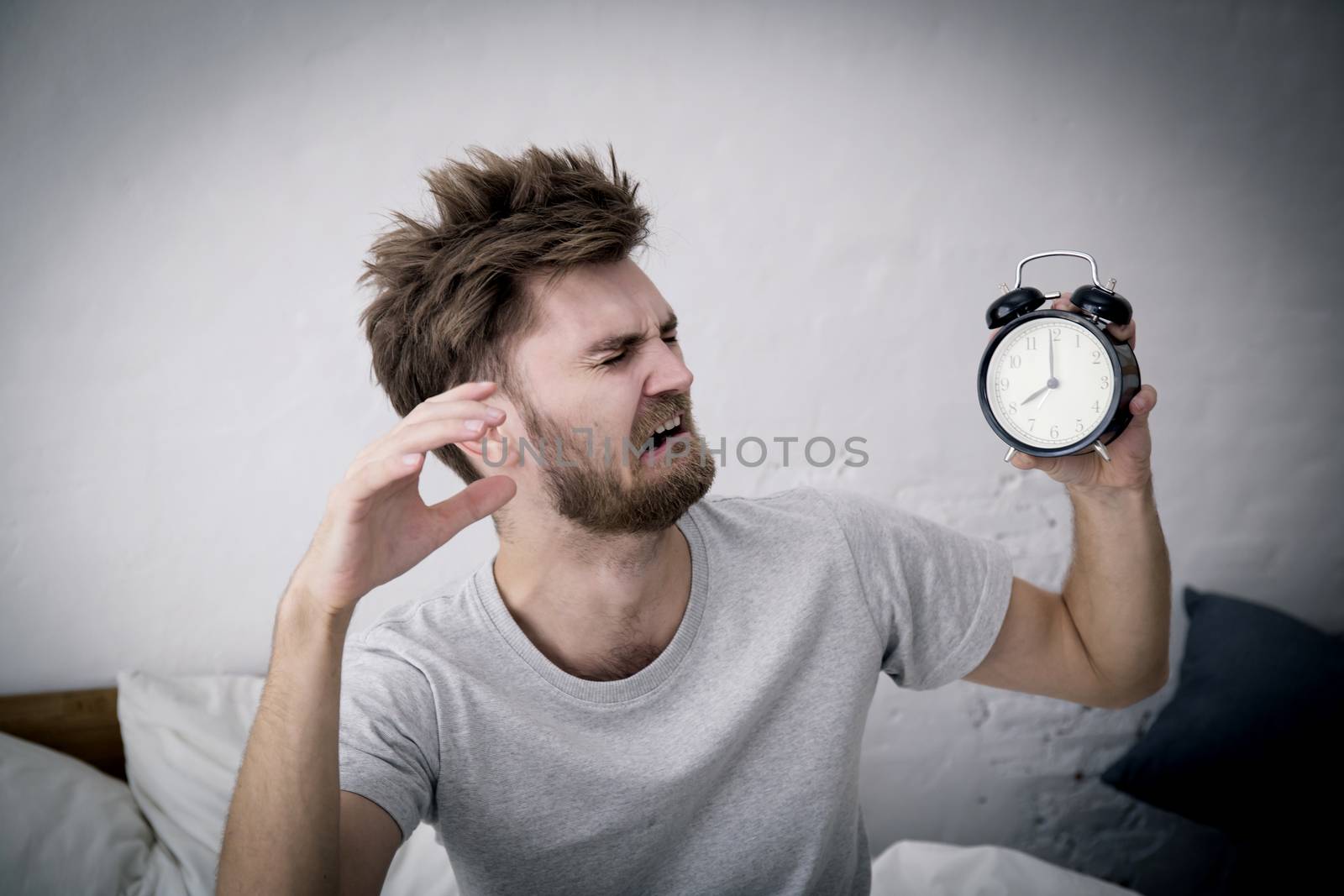 Portrait upset angry young man screaming at alarm clock on bedro by nnudoo