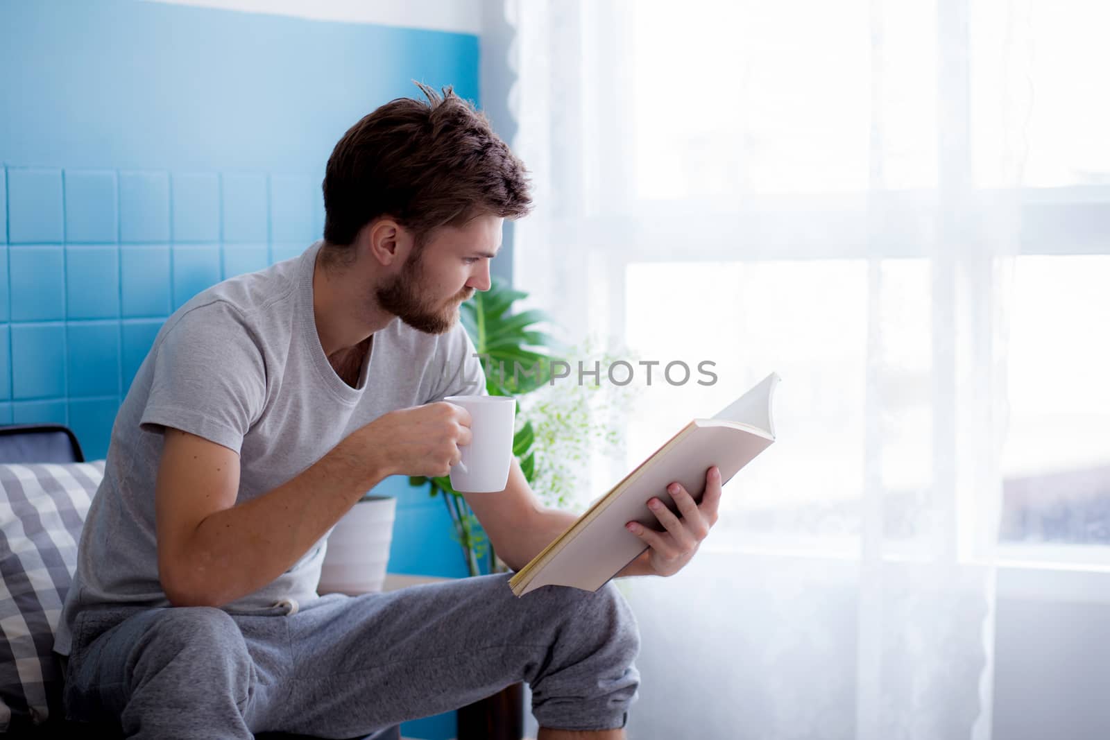 Young man reading book and drinking coffee on sofa in the living room