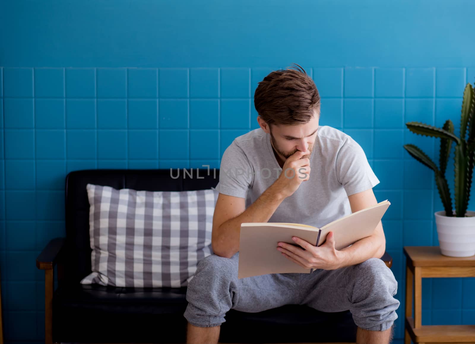 Young man reading book on sofa in the living room.