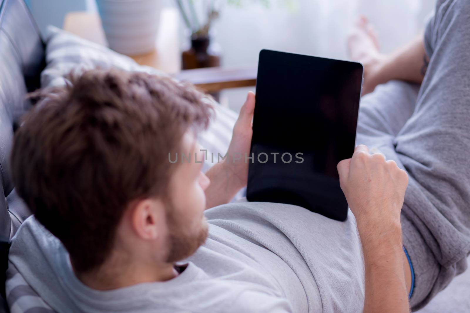Happy man watching media content in a tablet sitting on a couch  by nnudoo