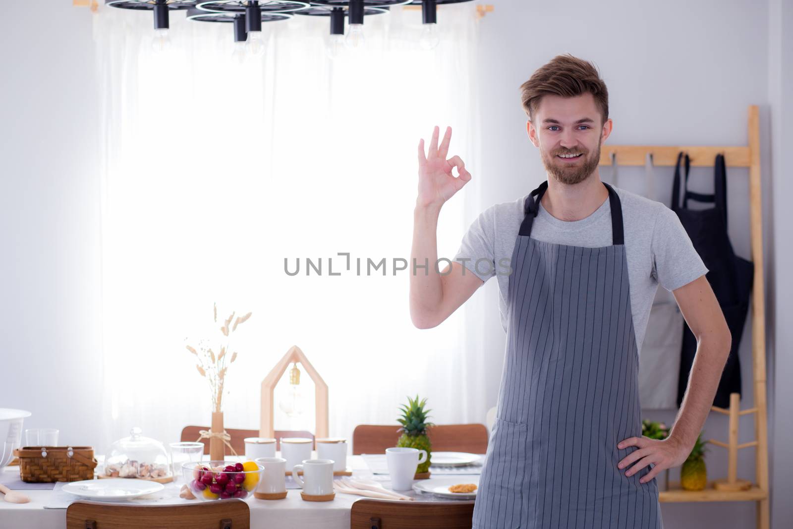 portrait of a smiling male cook gesturing okay sign in the kitch by nnudoo