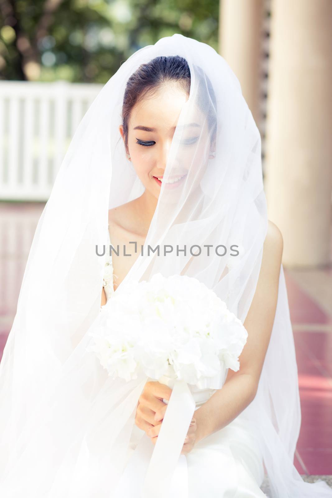 Portrait of a beautiful bride covering her face with a veil. Bright makeup with hand hold flower