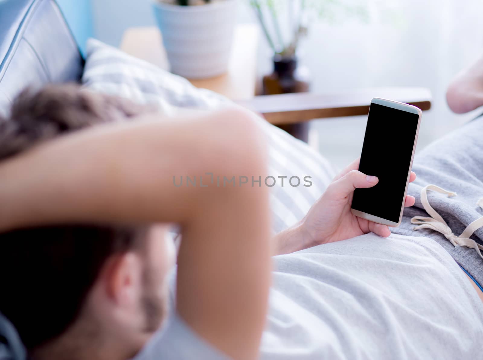 Happy man watching media content in a smart phone sitting on a couch at home, Top side view mock up background