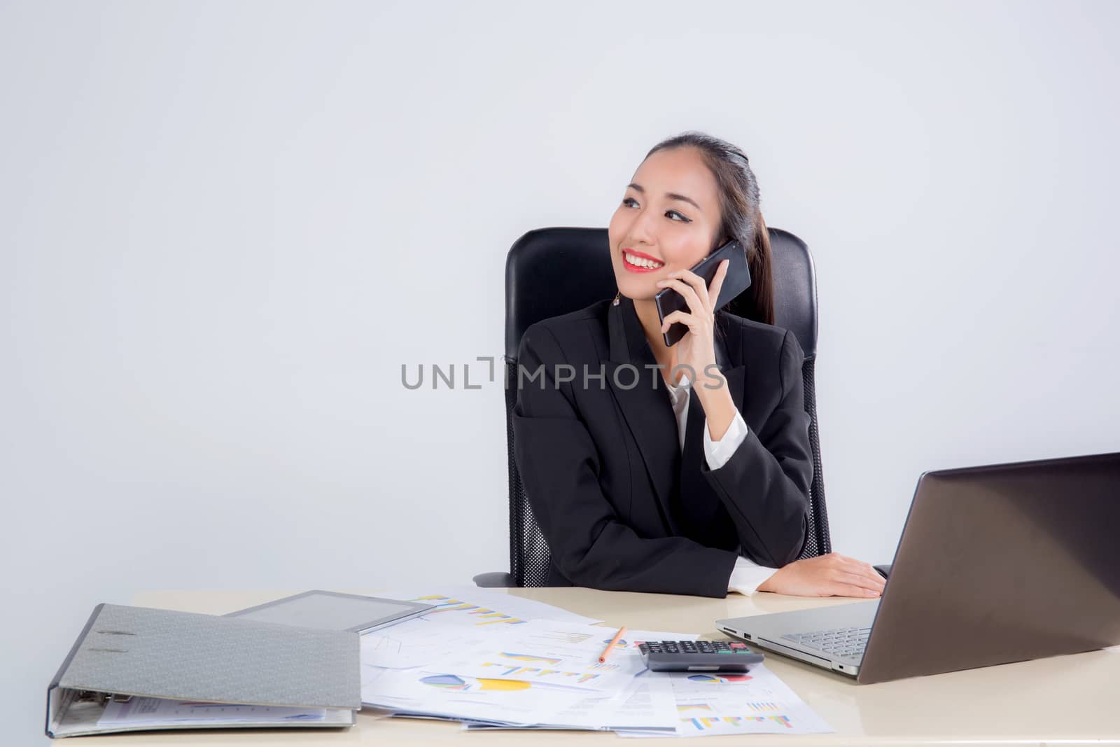 Young businesswoman working in office, typing, using computer and talking phone - Concentrated woman searching information online.