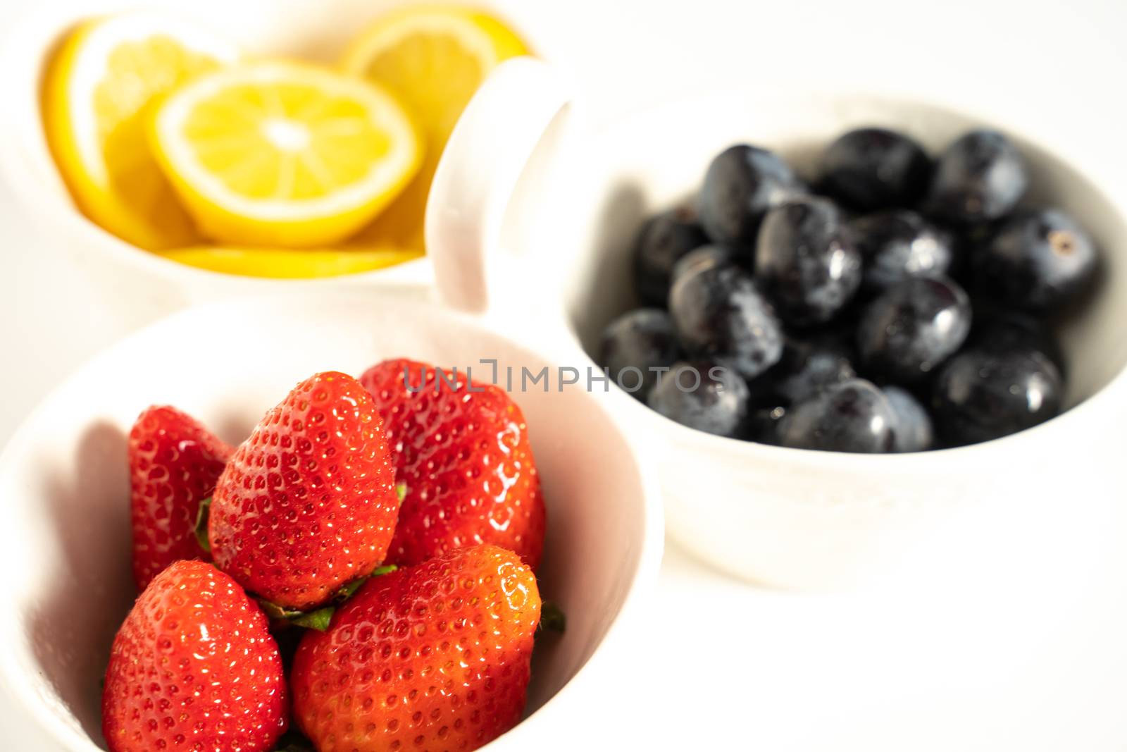 A serving dish filled with strawberries, lemon slices and black grapes against a plain white background