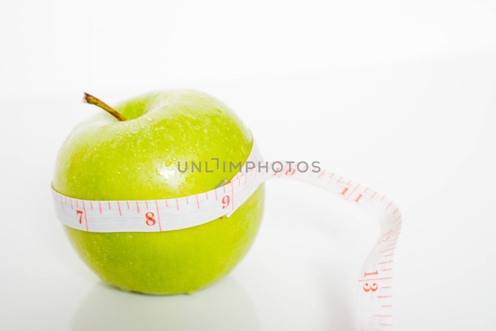 A granny smith green apple with a measuring tape wrapped around it against a plain white background