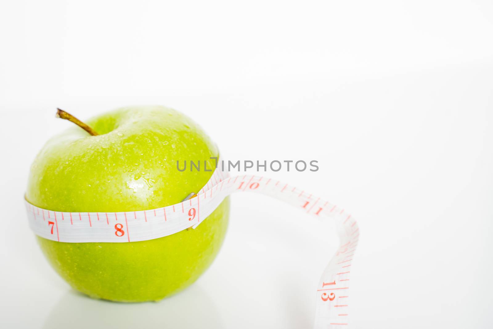 A granny smith green apple with a measuring tape wrapped around it against a plain white background