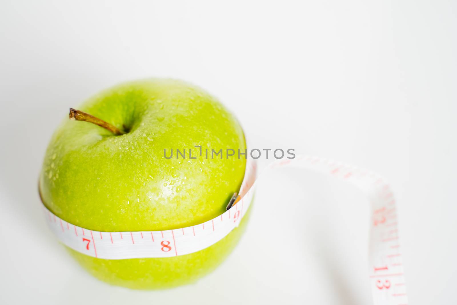 A granny smith green apple with a measuring tape wrapped around it against a plain white background