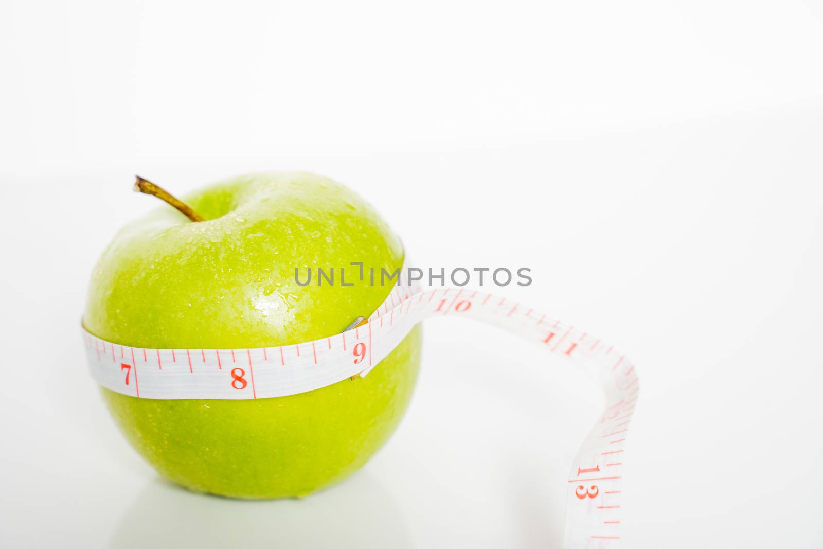 A granny smith green apple with a measuring tape wrapped around it against a plain white background