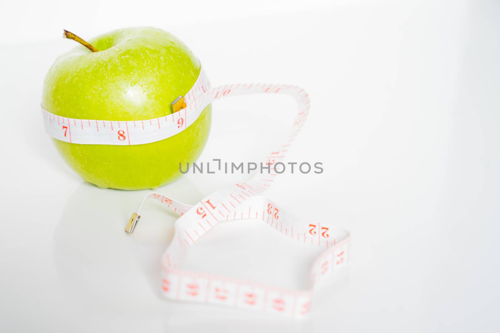 A granny smith green apple with a measuring tape wrapped around it against a plain white background