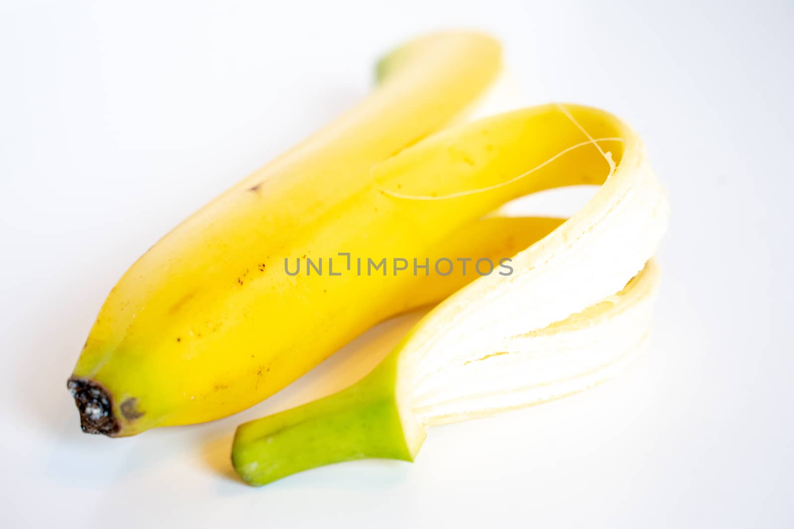 A Whole banana with the skin peeled back against a plain white background