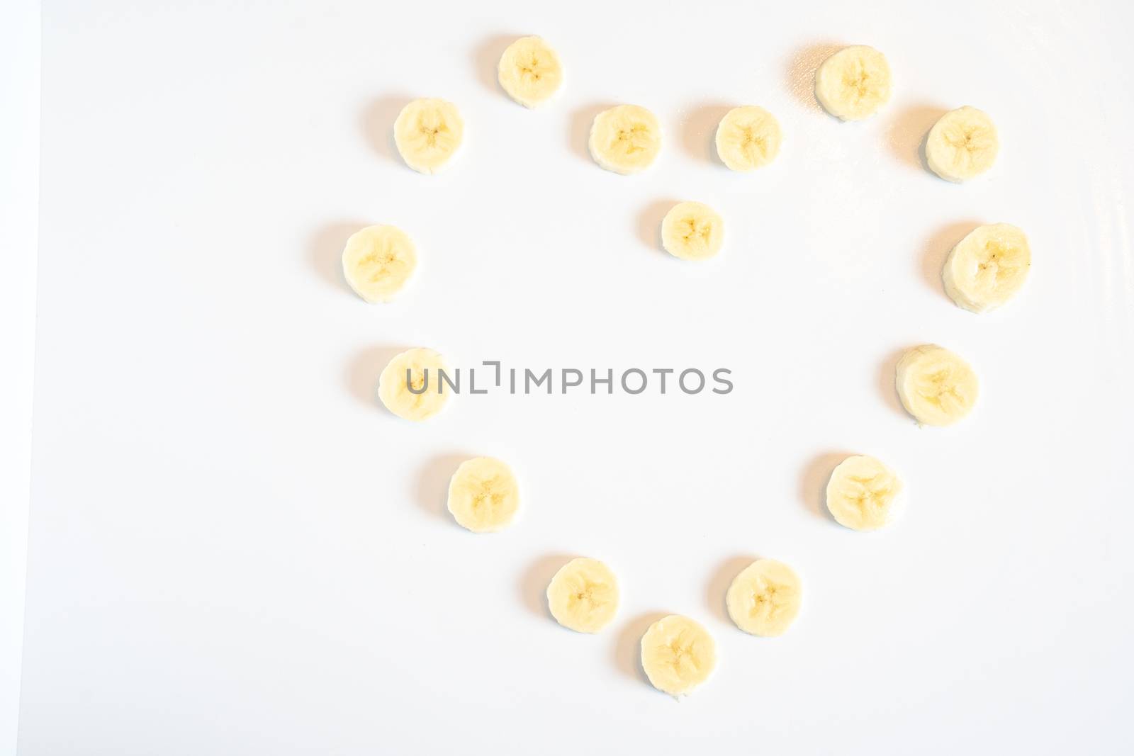 Slices of banana in the shape of a heart pattern against a plain white background