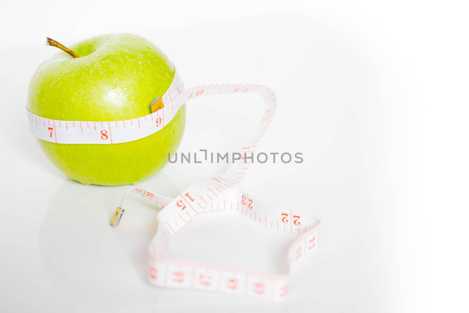 A granny smith green apple with a measuring tape wrapped around it against a plain white background