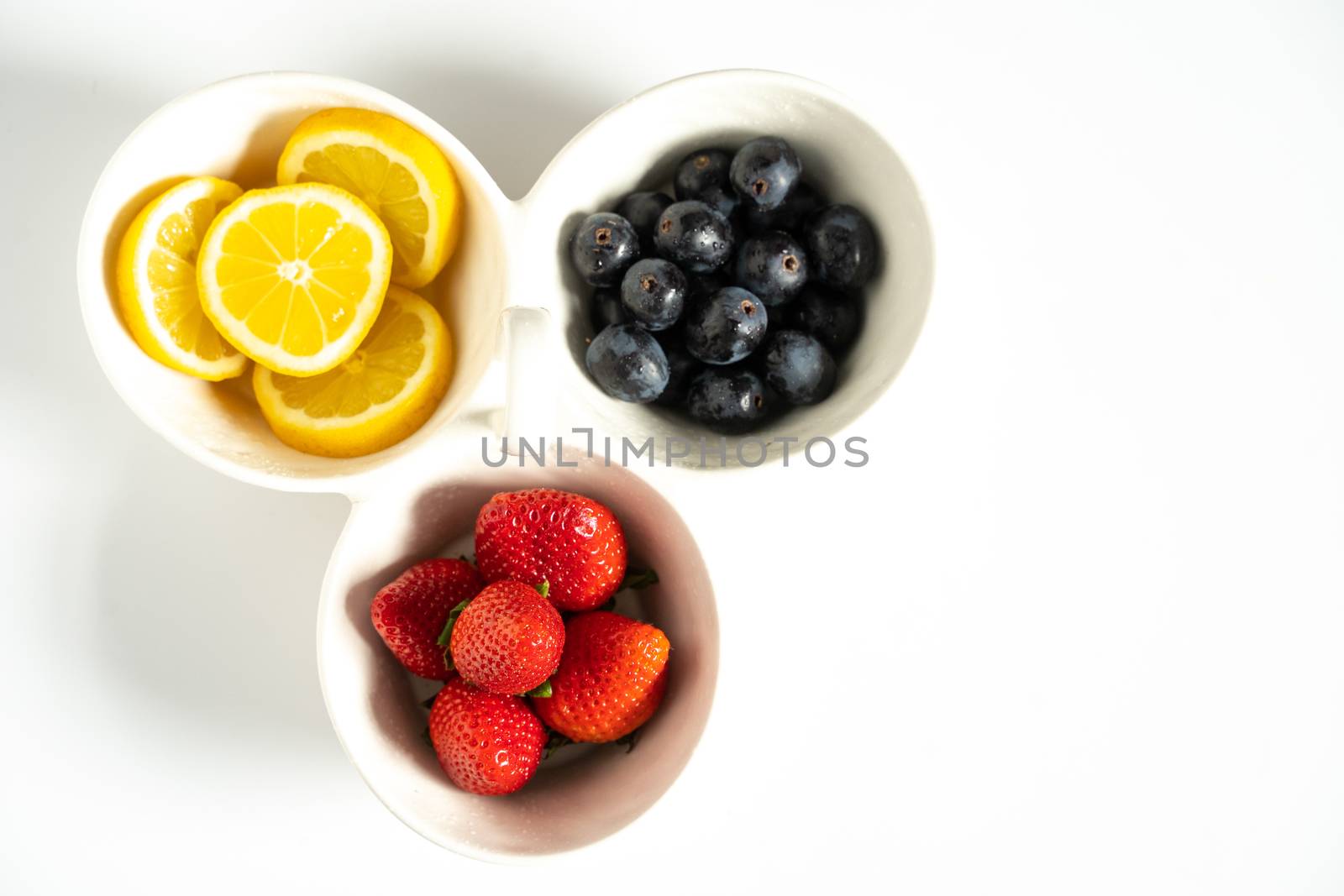 A serving dish filled with strawberries, lemon slices and black grapes against a plain white background