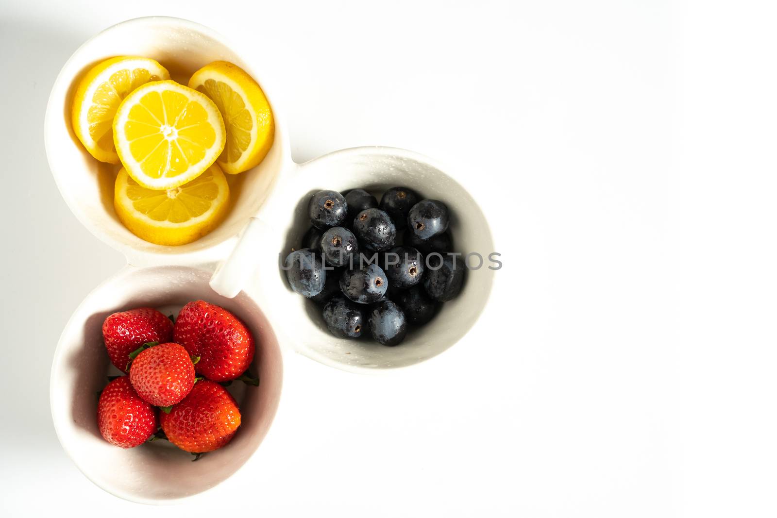 A serving dish filled with strawberries, lemon slices and black grapes against a plain white background