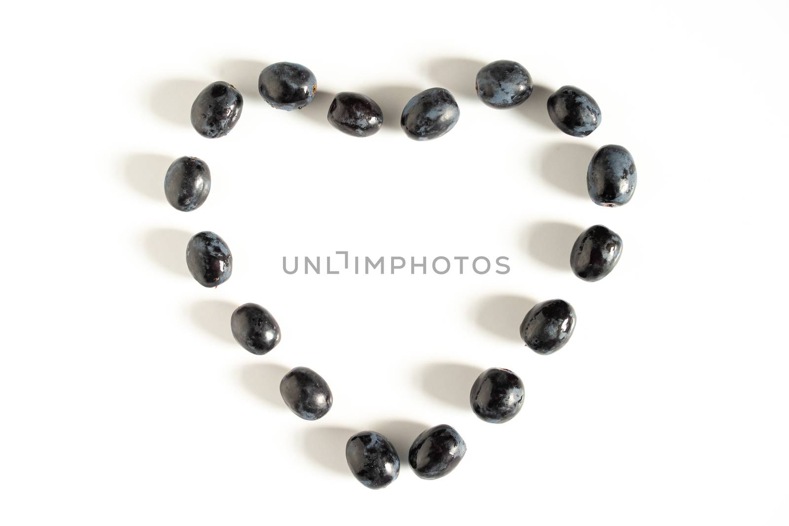 Some black grapes in the shape of a heart against a plain white background