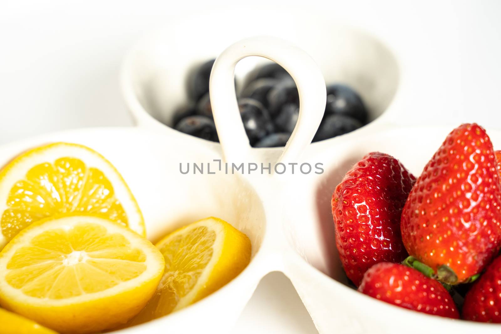 A serving dish filled with strawberries, lemon slices and black grapes against a plain white background