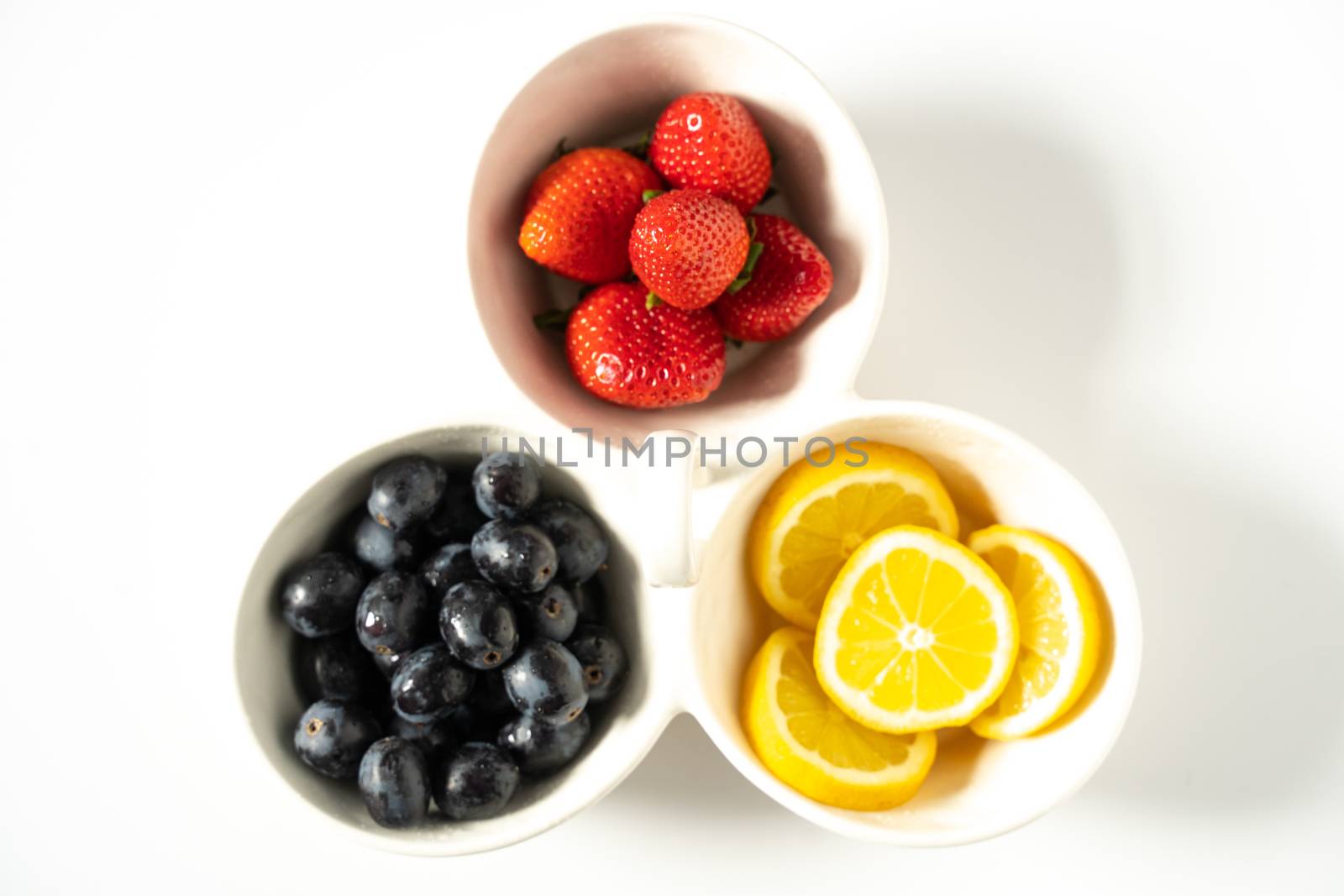 A serving dish filled with strawberries, lemon slices and black grapes against a plain white background